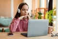 E-education, online lessons concept. Focused teen girl in headset looking at laptop screen, sitting at table at home