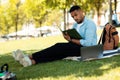 E-learning concept. African american male student preparing for lecture, using laptop and taking notes, sitting in park Royalty Free Stock Photo