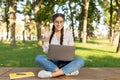 E-learning. Happy female student with laptop attending online lecture, waving hand at webcam, sitting on bench outdoors Royalty Free Stock Photo