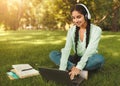 E-learning. Indian female student using laptop and wearing wireless headphones, watching educational lecture outdoors Royalty Free Stock Photo