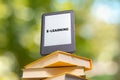 E-learning and reading. E-book reader is at the top of the stack of books. The park is blurred in the background. Close up. Royalty Free Stock Photo