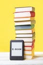 E-learning and reading. E-book and a stack of books on a yellow background. Vertical. Concept of education and electronic gadgets Royalty Free Stock Photo