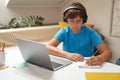 E-learning. Smart little boy in headphones using laptop while studying online, sitting at the table in his room Royalty Free Stock Photo