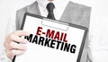 e-mail marketing inscription on a notebook in the hands of a businessman on a gray background, a man points with a finger to the