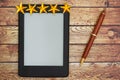 An e-reader on a wood desk with a pen and five gold stars Royalty Free Stock Photo