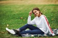 Side view. Positive girl in casual clothes with her laptop sits on green grass