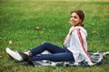 Side view. Positive girl in casual clothes with her laptop sits on green grass