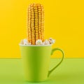 An ear of corn is sticking out of a green cup, as if it is growing, popcorn is scattered, concept Royalty Free Stock Photo