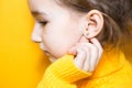 Ear piercing in a child - a girl shows an earring in her ear made of a medical alloy. Yellow background, portrait of a girl in Royalty Free Stock Photo