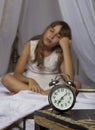 Early awakening. Alarm clock standing on bedside table. Wake up of an asleep young girl in bed on a background