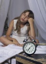 Early awakening. Alarm clock standing on bedside table. Wake up of an asleep young girl in bed on a background