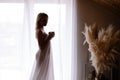 Early awakening morning magic. woman in sheet stands by the window drinking coffee from a mug.