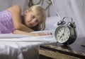 Early awakening. Wake up of an asleep young girl stopping alarm clock on a bed in the morning