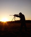 The early bird gets the worm. A silhouette of a man aiming with his rifle that is held up by a tripod in the outdoors at Royalty Free Stock Photo