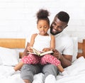 African american man reading book with his cute little daughter Royalty Free Stock Photo