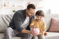 Early financial education. Cute little boy putting coin into piggy bank, daddy teaching his son to keep and safe money
