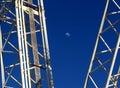The early moon seen between the steel structure of two crane booms