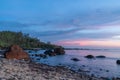 .Early morning on the beach with many pebbles and volcanic rocks, forest canopy and cloudy with the orange yellow light of dawn.