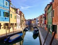 Early morning in Burano, Italy along a canal full of small boats and rows of colourful old attached homes.