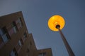 Early in morning round-shaped lantern on black holder was lit against blue twilight sky on upper floors of yellow building