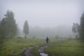 In the early morning in the fog  a mushroom picker boy with a basket is walking along the road Royalty Free Stock Photo