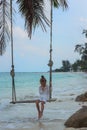 Early in the morning the girl in white dress swinging on swing on the beach deep in thought