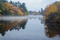 Mist hovers along a lake reflecting a New England autumn. Royalty Free Stock Photo