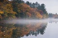 Mist hovers along a lake reflecting a New England autumn. Royalty Free Stock Photo
