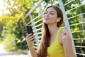 Early morning portrait of a happy young fitness girl sitting in the park enjoying listening to music using mobile phone with Royalty Free Stock Photo