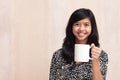 Beautiful asian girl holding a white mug and smiling to the camera