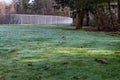 Early morning sun in a park with dew covered grass, woods, and fence around a sports field Royalty Free Stock Photo