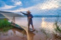 In the early morning before sunrise, an Asian fisherman on a wooden boat casts a net for catching freshwater fish in a natural Royalty Free Stock Photo