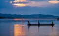 In the early morning before sunrise, an Asian fisherman on a wooden boat casts a net for catching freshwater fish in a natural Royalty Free Stock Photo