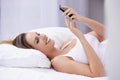 Early morning text messages...An attractive young woman reading a text message while lying in bed. Royalty Free Stock Photo