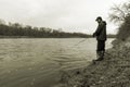 Early spring fisherman standing on the bank of a fast flowing ri