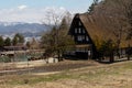 Early spring scenic landscape photograph of a traditional thatched roof house in rural Japan next to a rice paddy