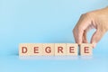 Earn a college degree concept. Human hand completing the word degree on wooden blocks.