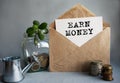 EARN MONEY text is written on white paper on an antique envelope, which lies on the table along with a stack of coins, a glass jar Royalty Free Stock Photo