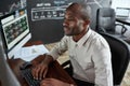 Earn more and count more. Cheerful african male trader sitting by desk and studying analytical reports using pc in the