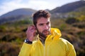 Earphones, outdoors and man in nature, mountain and flora for exercise or training. Raincoat, music and workout for Royalty Free Stock Photo