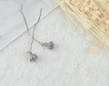 Grey pendant flower earrings in the shape of a flower.Earrings are flanked by cardboard, floral specimens and other ornaments