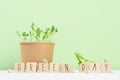Earth day background - young peas sprouts potted in craft pot with lettering `green day` on wood cubes, seeds on white wood.