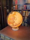 Earth globe lamp lit on a wooden table in a library.