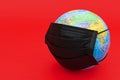 Earth globe model with black surgical mask isolated on red background. Royalty Free Stock Photo