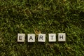 Earth written with wooden letters cubed shape on the green grass.