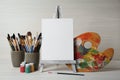 Easel with blank canvas, brushes, paints and palette on white wooden table Royalty Free Stock Photo