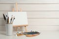 Easel with blank canvas, brushes, paints and palette on white wooden table. Space for text Royalty Free Stock Photo