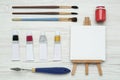 Easel with blank canvas, brushes and paints on white wooden table, flat lay. Space for text Royalty Free Stock Photo