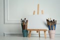 Easel with blank canvas and brushes on white wooden table Royalty Free Stock Photo