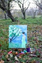 Easel with paints and painting on canvas in autumn park
